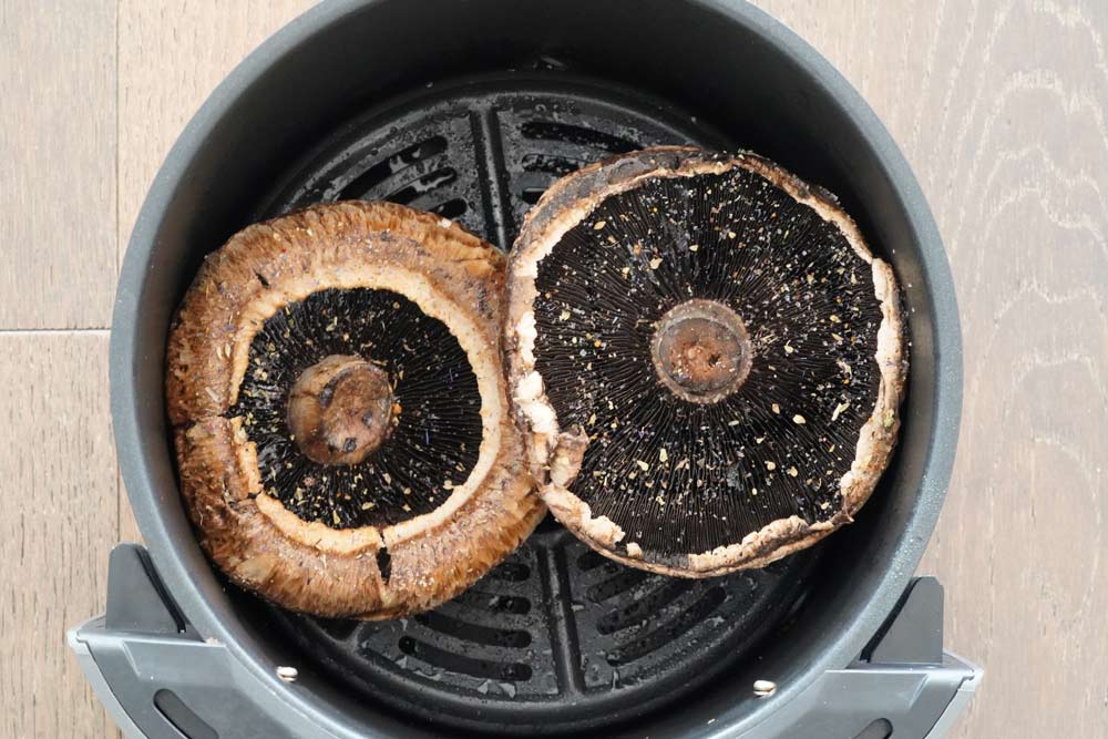 Two uncooked Portobello mushrooms in the air fryer basket