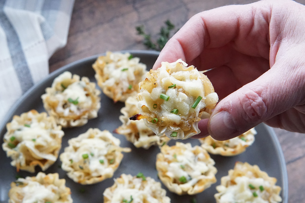 Holding up a French onion bite and more on a tray