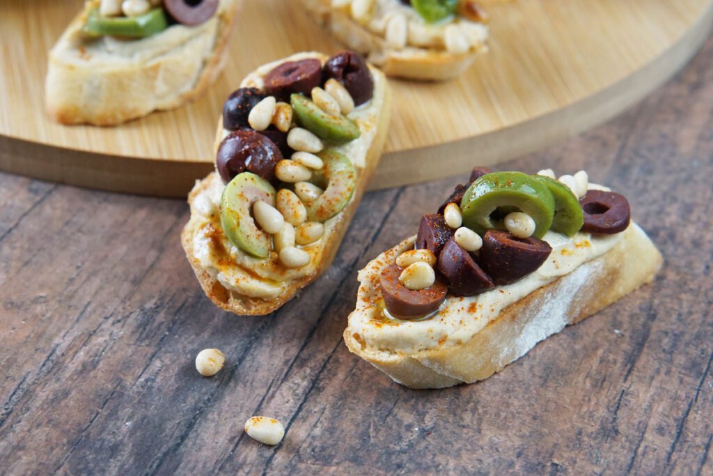Hummus crostini with olives and pine nuts